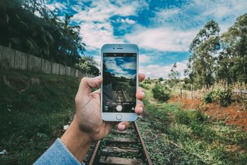 Hand holding iPhone in front of railroad tracks