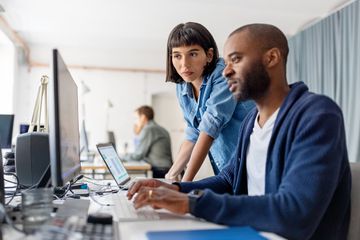 Two business people looking at desktop computer monitor and discussing new programme codes.