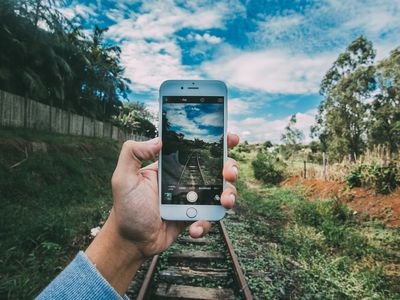 Hand holding iPhone in front of railroad tracks