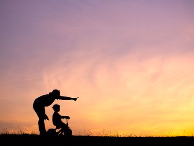 Silhouette Woman With Daughter Riding Bicycle On Field Against Orange Sky