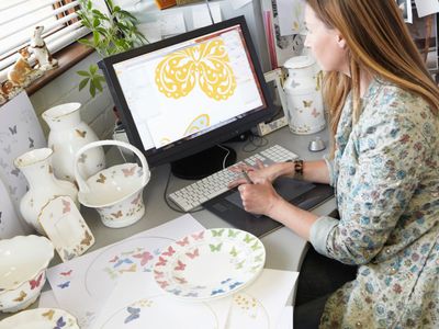 Woman doing graphic art on a computer surrounded by ceramics