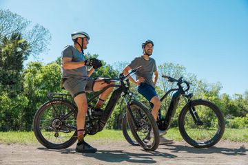 Two people sitting on Mod Black e-bikes on a dirt trail.