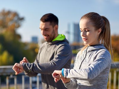 man and woman checking fitness trackers on wrists