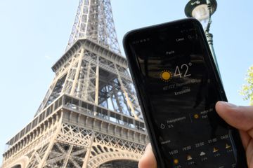 A person standing next to the Eiffel Tower holds a smartphone