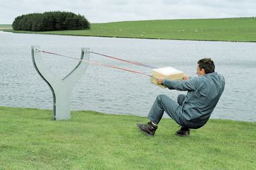 A man placing a large package in a big slingshot.