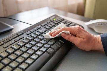 A person cleaning a keyboard with wipes