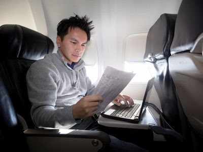 Person using laptop and reading newspaper on plane