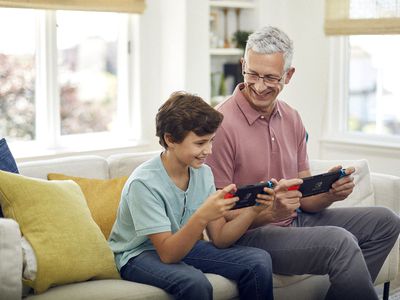 A man and a boy playing on two Nintendo Switch consoles.