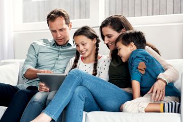 A father, mother, son, and daughter sitting on a sofa looking at data on an iPad.