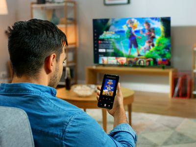 A man in a blue shirt sitting on a lounge and casting a Netflix show from his smartphone to his TV.