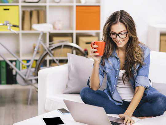 A woman looking at her laptop while sitting on a couch and holding a mug