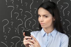 A person holding a phone in front of a blackboard of question marks