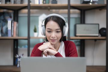 A woman wearing headphones sitting at a desk looking at a laptop