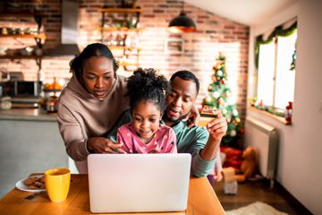 A family of three gathering around a laptop on a kitchen table