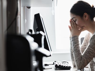 A woman is at a computer, with her head in her hands.