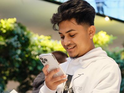 A young man wearing a white jumper holding a white Apple iPhone 15 Pro Max smartphone.