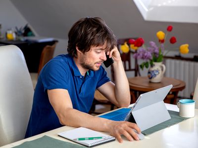 A man in a blue polo shirt looking at his Microsoft Surface Pro computer with a concerned look on his face.