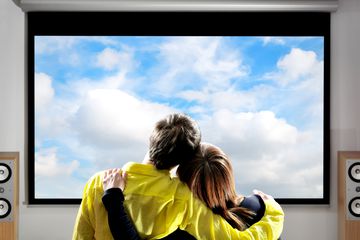 A couple watching a large monitor on a wall.