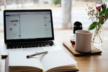 Notebook with pen open in front of computer