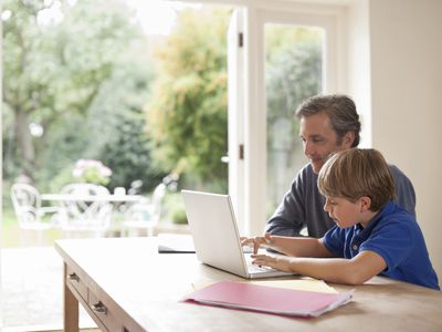 A parent and child working on a laptop computer in the kitchen.