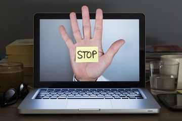 A hand with a stickynote that says STOP coming out of a laptop display