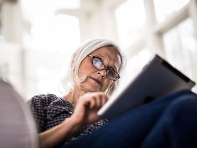 Someone sitting on a sofa, using an iPad tablet.