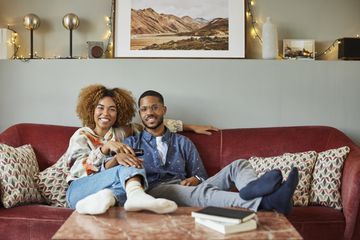 A couple sitting on a sofa smiling and watching TV