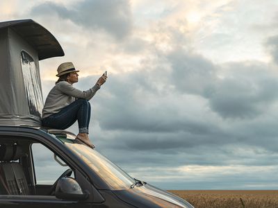 Woman sitting on top of a camper van, looking at her iPhone