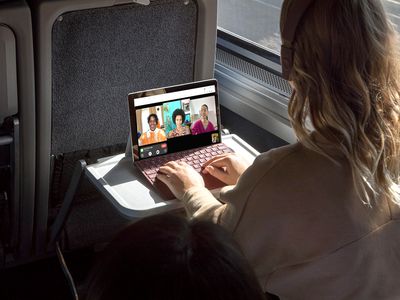 A woman sitting on a train using Apple FaceTime video chat on her Microsoft Surface Pro Windows laptop.