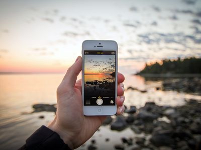 A person holding an iPhone taking a picture of the beach