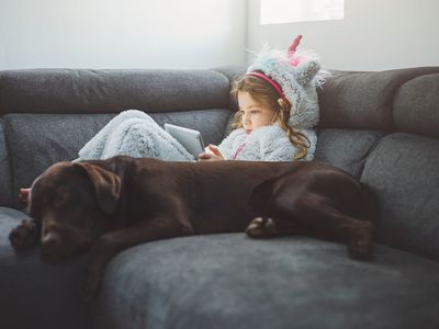 Young girl in a unicorn onesie using tablet, dog by her side