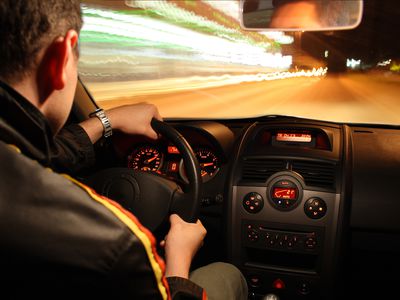 Man driving car fast at night, picture taken with long exposure of interior of car man driving