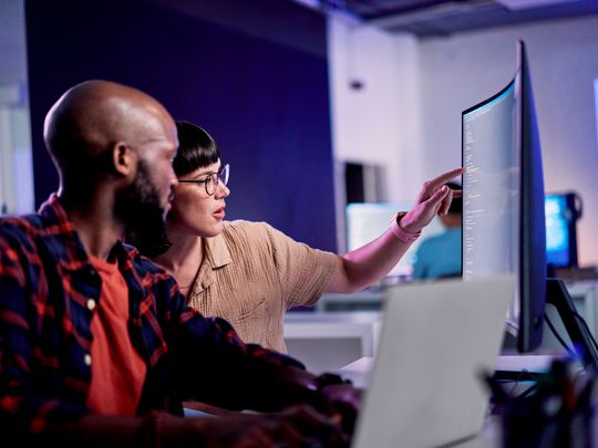 A man and woman in an office looking at a second monitor connected to a Windows 11 laptop computer.