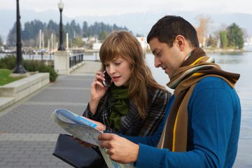 Couple reading map on waterfront, young woman using mobile phone