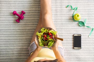 Overhead view of someone sitting with a bowl of salad and an smartphone.