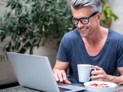 Man wearing glasses using an internet browser on his laptop in a cafe.