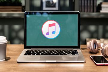 iTunes on laptop screen with coffee and headphones on desk