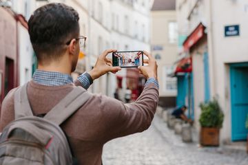 A man wearing a backpack and taking a photo with his smartphone while traveling internationally.