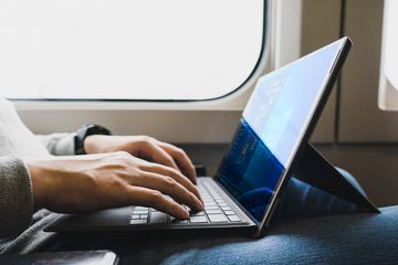 A man sitting on a train with a Microsoft Surface Pro laptop on his lap running Windows 11 that looks like Windows 10.