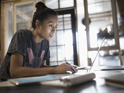 Focused Asian woman working at a laptop in a home office.