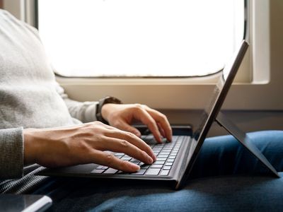 A man with an open Microsoft Surface Pro laptop tablet on his lap while sitting on a train.