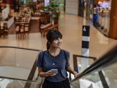 A smiling woman holding a phone and going up an escalator