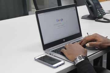 Person on laptop using Google next to mobile and landline phones