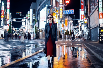 A stylish woman walks down a Tokyo street filled with warm glowing neon and animated city signage. She wears a black leather jacket, a long red dress, and black boots, and carries a black purse. She wears sunglasses and red lipstick. She walks confidently and casually. The street is damp and reflective, creating a mirror effect of the colorful lights. Many pedestrians walk about.