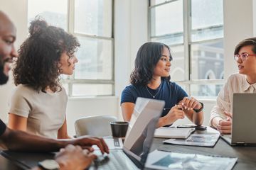 Several people in a business meeting, some using laptops.