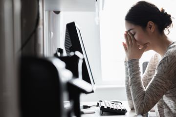 A woman is at a computer, with her head in her hands.