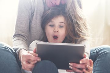 A young child sitting with their parent and using an iPad.