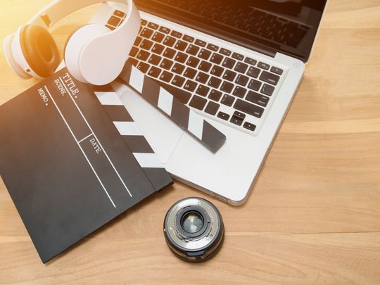 Clapboard, headphones, camera lens, and computer on a desk representing film making and video editing