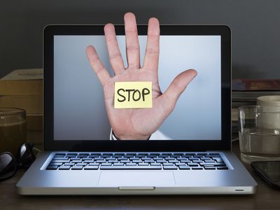 A hand with a stickynote that says STOP coming out of a laptop display