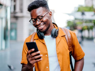 A man wearing an orange shirt, headphones, and glasses recording a video voicemail message via FaceTime on his iPhone.